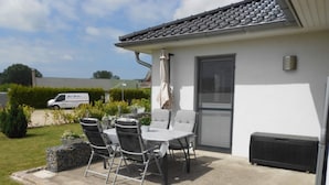 Une terrasse avec une table et des chaises, un bâtiment blanc et un fourgon en arrière-plan.