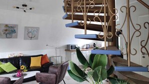 Een woonkamer met een zwarte leren bank, een salontafel en een plant. Er is een trap met een decoratieve balustrade.