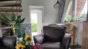 Een moderne woonkamer met een leren bank, een eettafel met een vaas vol zonnebloemen en druiven, en een keuken in de achtergrond.