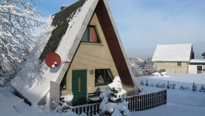 Een huis bedekt met sneeuw, met een schuin dak, een schotelantenne en een hek met puntjes.