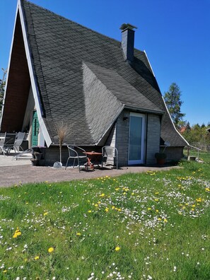 A house with a steeply pitched roof, a stone chimney, and a small patio area with outdoor furniture. - Familienferienhaus in Huttenrode (Blankenburg)