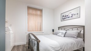 A bedroom with a bed, a window with blinds, a radiator, a wall-mounted artwork, and a wooden floor. - Platform Avenues Area Apartments (Hull)