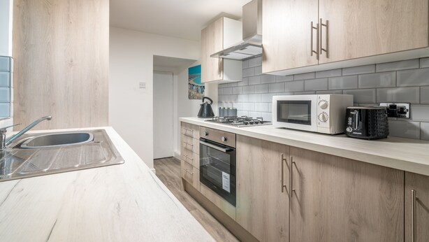 A modern kitchen with wooden cabinets, a stainless steel sink, a microwave, and a gas stove. - Platform Avenues Area Apartments (Hull)