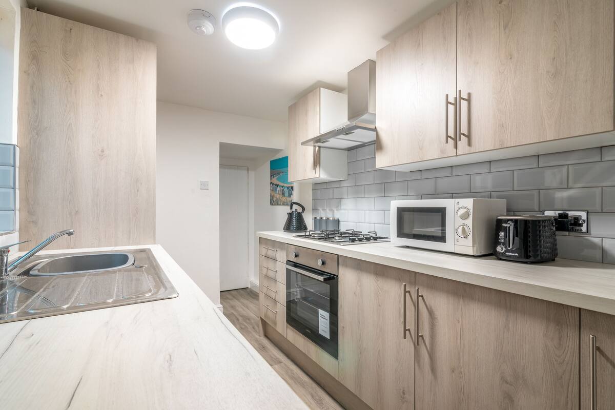 A modern kitchen with wooden cabinets, a stainless steel sink, a microwave, and a gas stove.