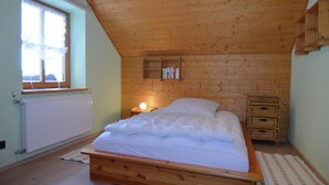 Ein Schlafzimmer mit einem hölzernen Bett, einem Fenster mit Vorhängen, einem Nachttisch mit einer Lampe und einer Heizung.