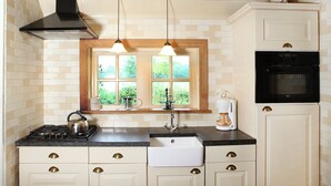 A kitchen with a stove, sink, and window with a view of greenery. - Cozy Apartment in Enschede near Forest (Enschede)