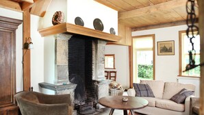 A cozy living room with a fireplace, wooden furniture, and a view of greenery outside. - Cozy Apartment in Enschede near Forest (Enschede)