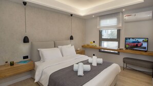 A modern hotel room with a large bed, a TV, a window, and a wooden nightstand. - Acropolis Golden Suites | 2nd Floor (Athina)