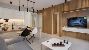 A modern living room with a sofa, coffee table, and a TV mounted on a wooden wall. - Acropolis Golden Suites | 2nd Floor (Athina)