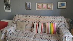 Un salon avec un canapé à pois, un coussin rouge et trois tableaux encadrés accrochés au mur.