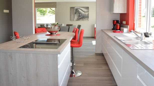 Una cocina moderna con una isla central, taburetes rojos y un ventanal que proporciona luz natural.