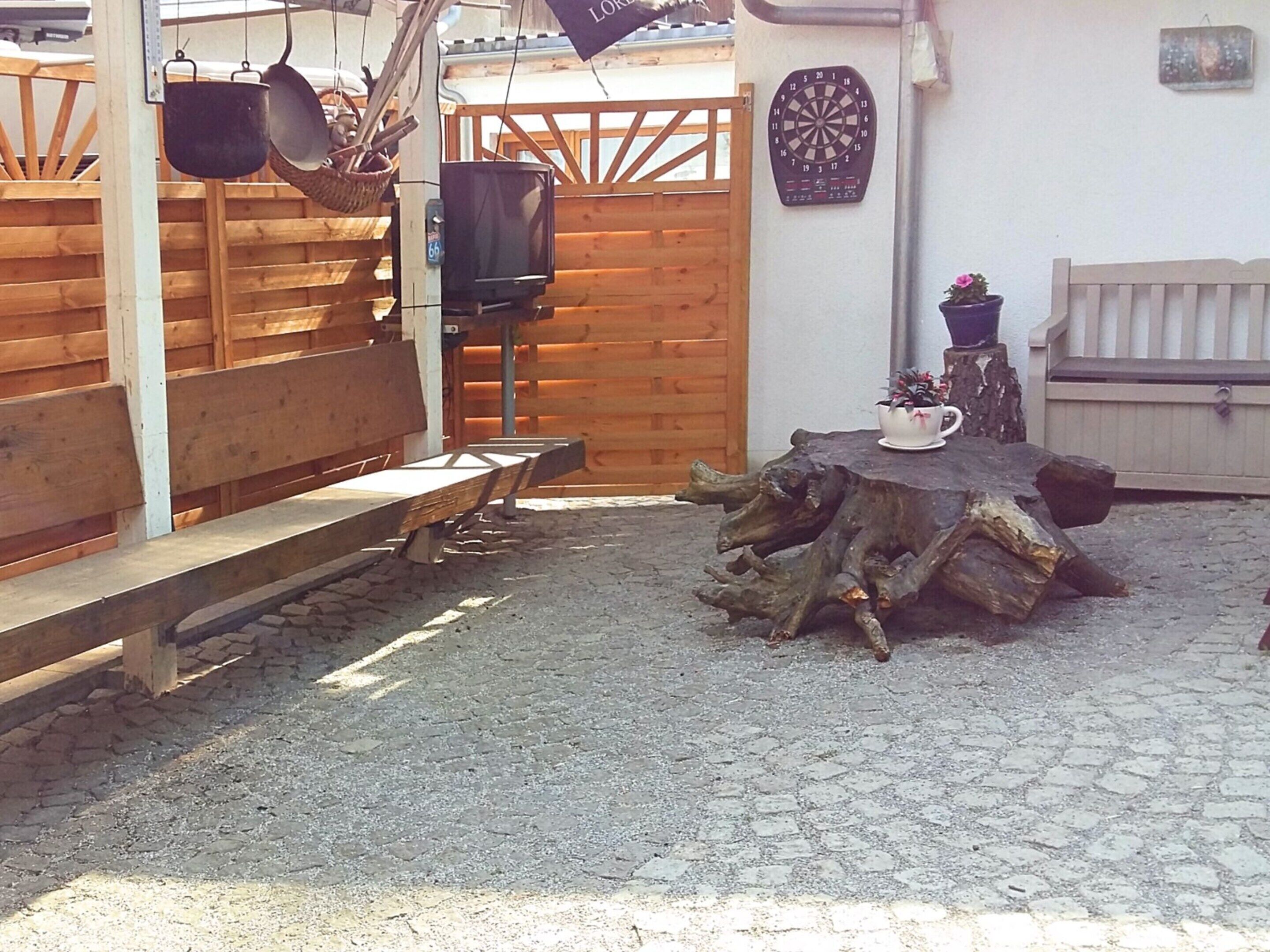 Zona d'estar a l'exterior d'estil rústic, amb bancs de fusta i una taula envoltada per una tanca de fusta.