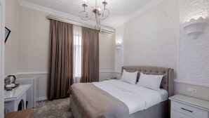 Une chambre à coucher comprenant un lit, une table de chevet, une chaise, un bureau et une fenêtre avec des rideaux.
