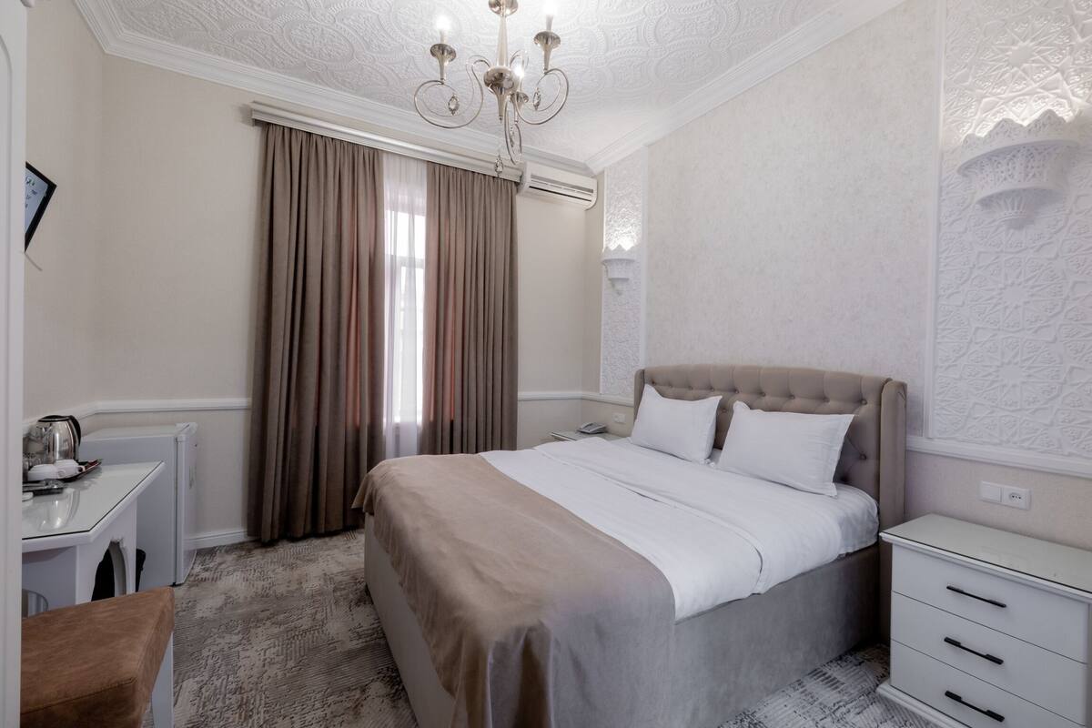 A bedroom with a bed, a bedside table, a chair, a desk, and a window with curtains.