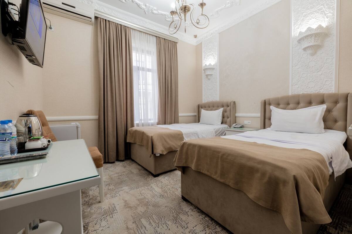 A hotel room with two beds, a desk, a TV, and a chandelier.