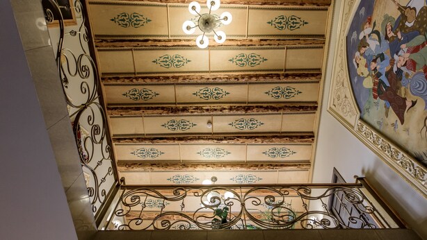 Un plafond richement décoré, orné de motifs complexes, et un luminaire central.