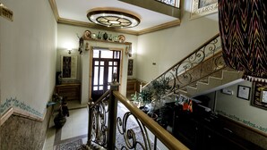 Un magnifique escalier orné de balustrades travaillées, un lustre et une vue sur l’étage supérieur.