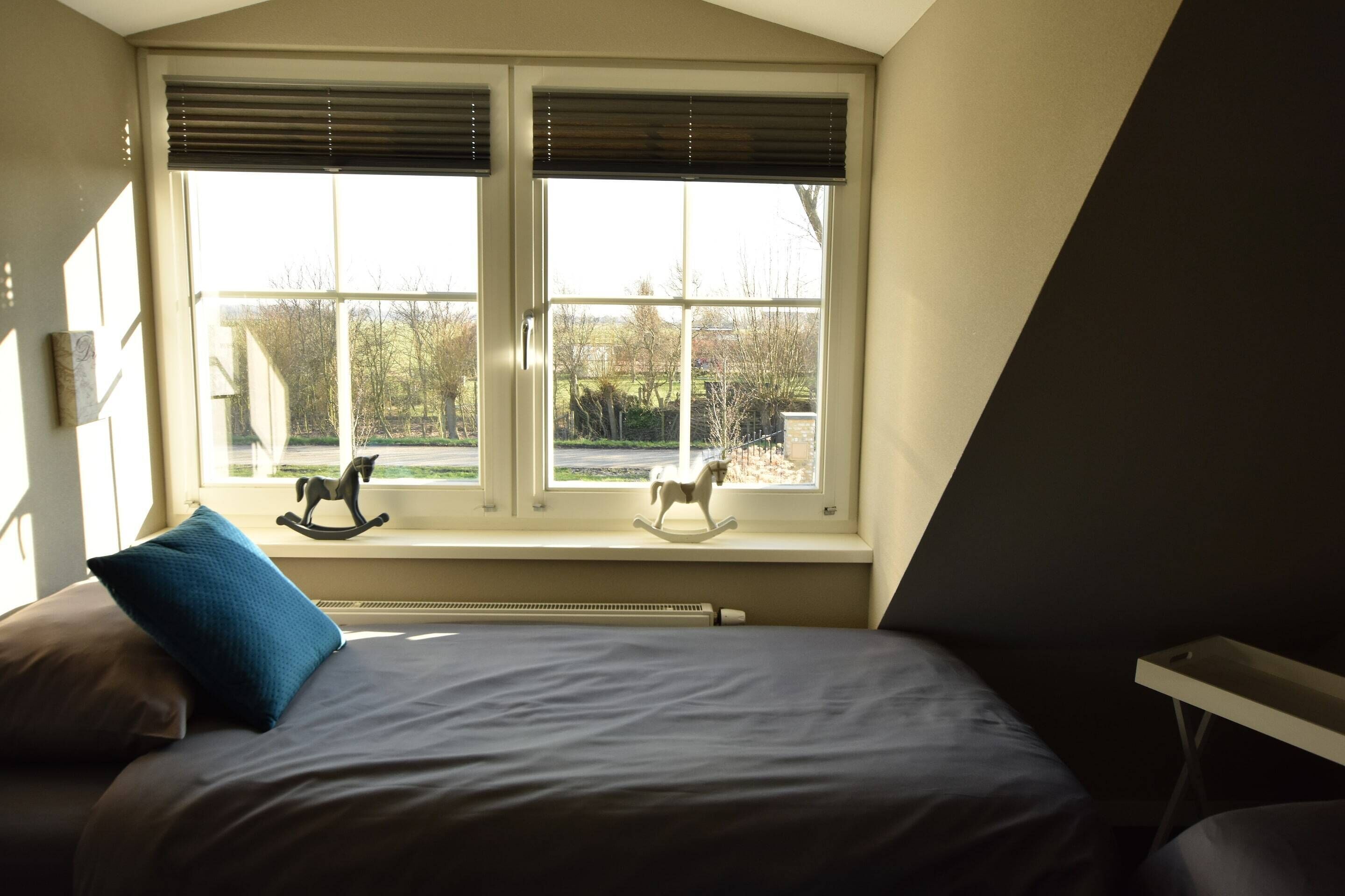 Un dormitorio con una cama, dos caballos balancines en el alféizar de la ventana y un radiador debajo.