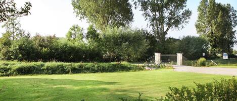 A well-maintained grassy area with a metal gate, surrounded by trees and shrubs.