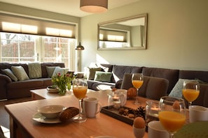 Een ontbijtruimte met een houten tafel, gedekt met kommen, glazen sinaasappelsap en gebak.