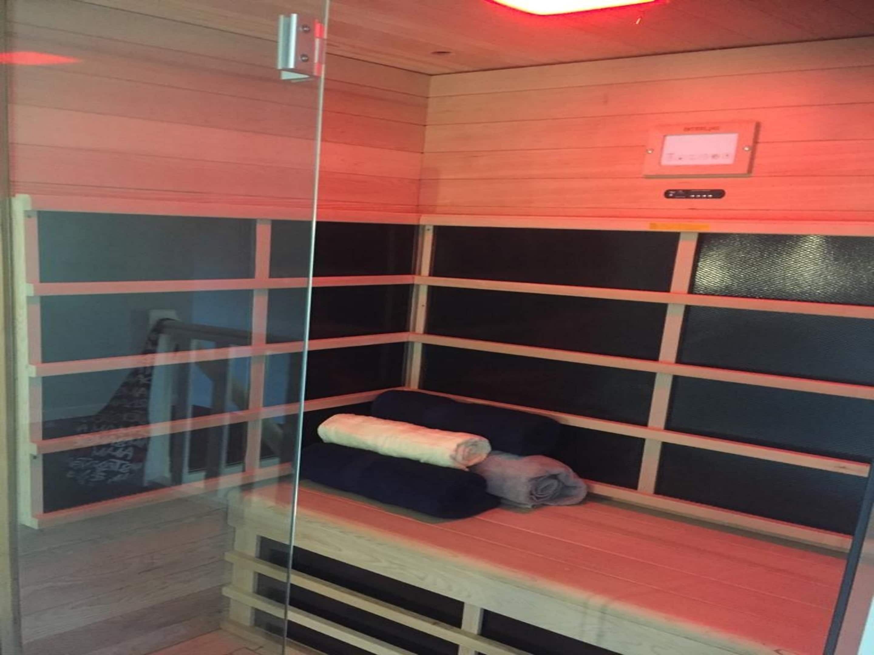 Eine Sauna mit Glastrennwand, Holzbänken und Bedienfeld.