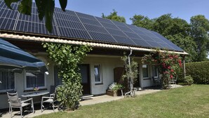 Uma casa com telhado solar, um pátio com móveis de jardim e um jardim com parede coberta por hera.