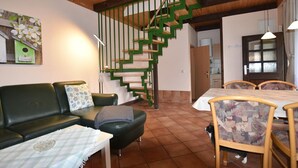 Uma sala de estar acolhedora com uma escada espiral verde, uma área de jantar com cadeiras estampadas e um sofá verde com almofadas.