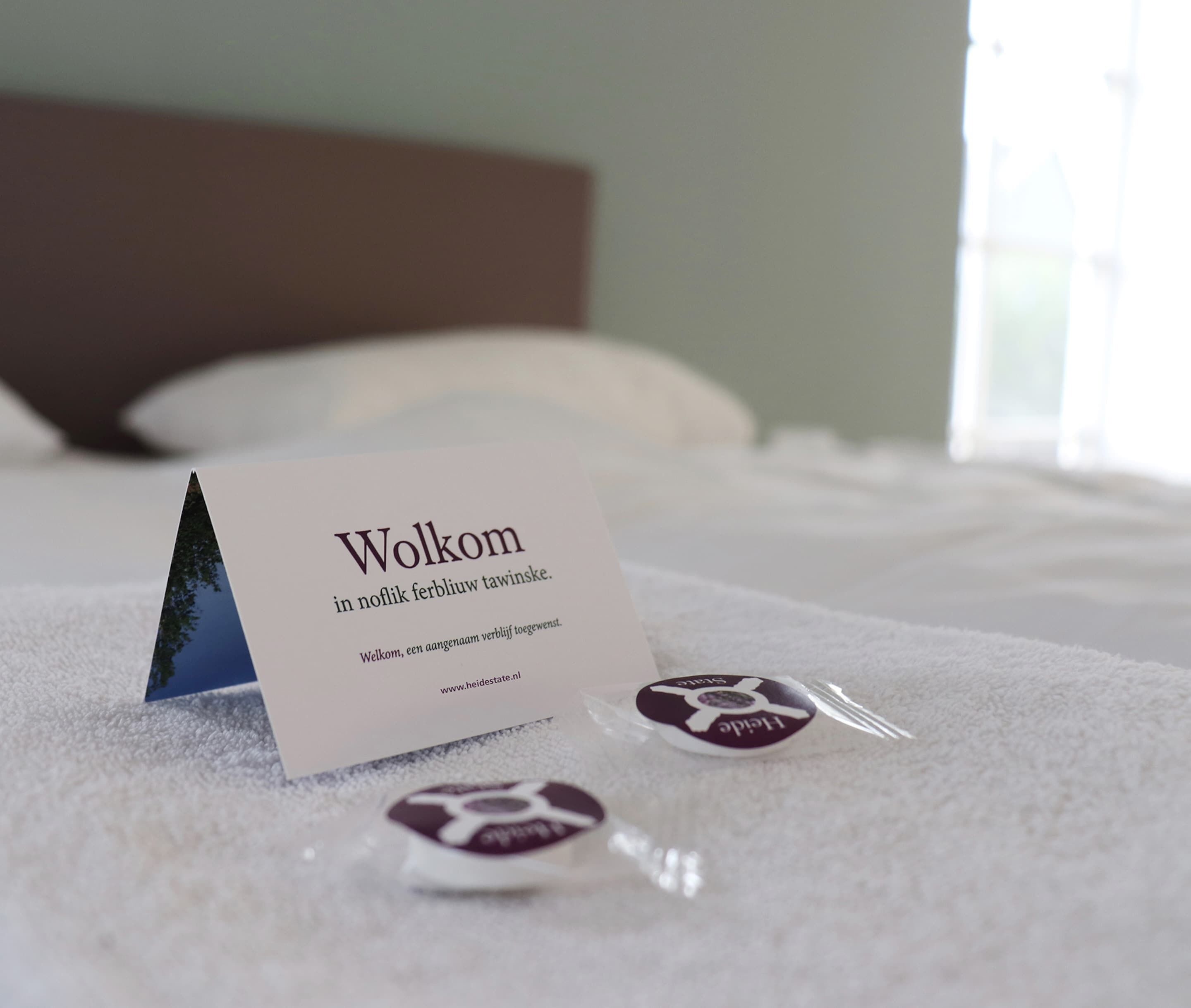 Une chambre d’hôtel avec un lit, une carte de bienvenue et deux petits objets posés sur le lit.