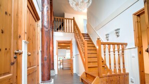 A wooden staircase with a railing leading to a second floor, flanked by wooden doors and a stone column. - Spacious Farmhouse With Sauna, Hottub (Noardburgum)
