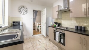A modern kitchen with a sink, stove, and cabinets. There is a dining area with a table and chairs visible through an open door. - Platform Fishing Quarter Apartments (Hull)
