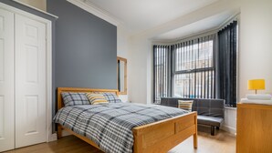 A bedroom with a wooden bed, a bench, a desk, a window with curtains, and a wardrobe. - Platform Fishing Quarter Apartments (Hull)