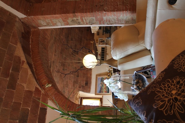 A room with a brick wall, a white sofa, a decorative lamp, and a plant. - Not available (Montescudaio)