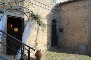 An old building with a rustic exterior, a metal staircase, and a large terracotta pot. - Not available (Montescudaio)