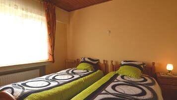 A bedroom with two single beds, wooden headboards, a nightstand with a lamp, and a window with curtains.