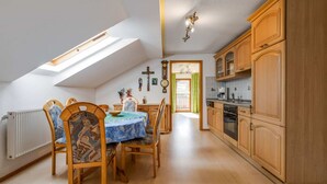 A dining area with a table and chairs, wooden cabinets, a kitchen with appliances, and a skylight. - Bauernhof in Spandlberg am Hohe Bogen (Neukirchen Beim Heiligen Blut)