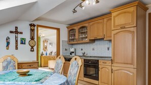 A kitchen with wooden cabinets, a dining table with chairs, a clock, and a cross on the wall. - Bauernhof in Spandlberg am Hohe Bogen (Neukirchen Beim Heiligen Blut)