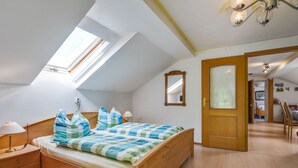 A bedroom with a sloped ceiling, a skylight, a wooden bed, a bedside table, a mirror, and a door leading to another room. - Bauernhof in Spandlberg am Hohe Bogen (Neukirchen Beim Heiligen Blut)