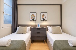A hotel room with two beds, a nightstand, a lamp, and artwork on the wall. - Sweett | Sepulveda XI (Barcelona)