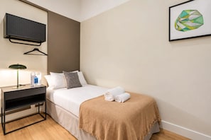 A hotel room with a bed, a desk with a lamp, a hanging TV, and a framed picture on the wall. - Sweett | Sepulveda XI (Barcelona)