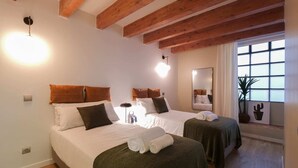 A hotel room with two beds, wooden beams, a large window, and a mirror. - Sweett | Verdi Baixos (Barcelona)