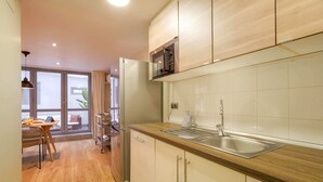 A modern kitchen with wooden cabinets, a stainless steel sink, and a built-in microwave. - Sweett | Verdi Baixos (Barcelona)