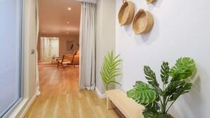 A hallway with a wooden floor, a bench, and two potted plants. - Sweett | Verdi Baixos (Barcelona)