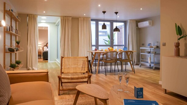 A modern living room with a dining area, wooden furniture, and a large window with curtains. - Sweett | Verdi Baixos (Barcelona)