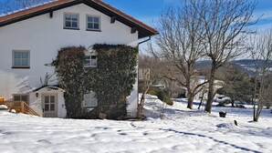 A white house with a red roof, surrounded by snow-covered ground and leafless trees. - Tranquil Garden Apartment (Regen)