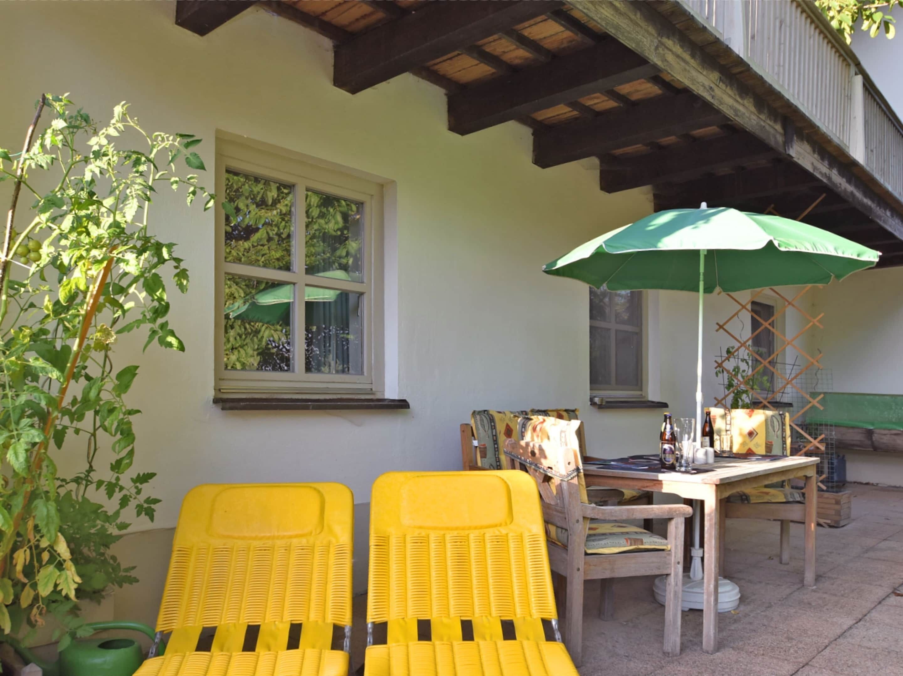 A patio with yellow chairs, a table, and a green umbrella.