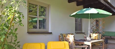 A patio with yellow chairs, a table, and a green umbrella.