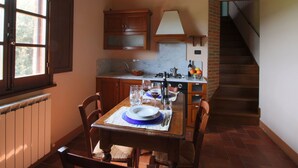 Ein Essbereich mit Tisch für vier Personen, eine Küche mit Gasherd und eine Treppe, die zu einer oberen Etage führt.