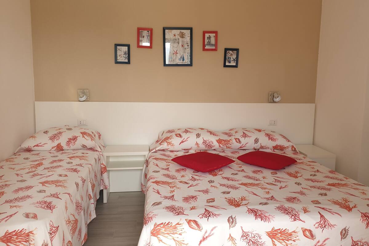 A room with two beds, each with red pillows and a leaf-patterned bedspread. There are four framed pictures on the wall above the beds.