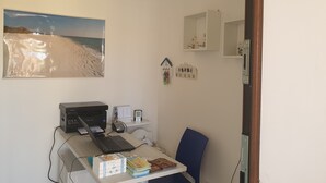 A room with a desk, a laptop, a printer, a small shelf with books and snacks, a wall-mounted calendar, and a beach-themed poster. - Caletta sul Mare (Siniscola)