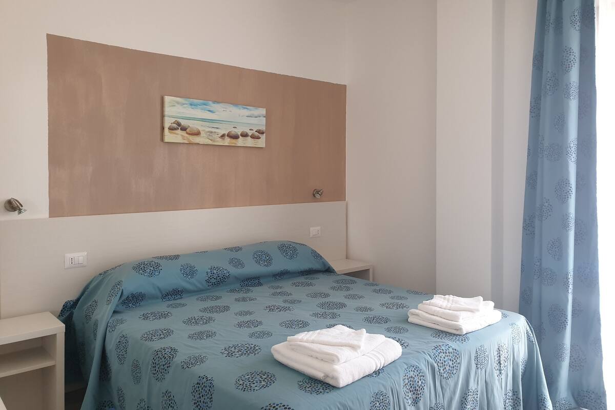 A bedroom with a bed, a painting, and a curtain.